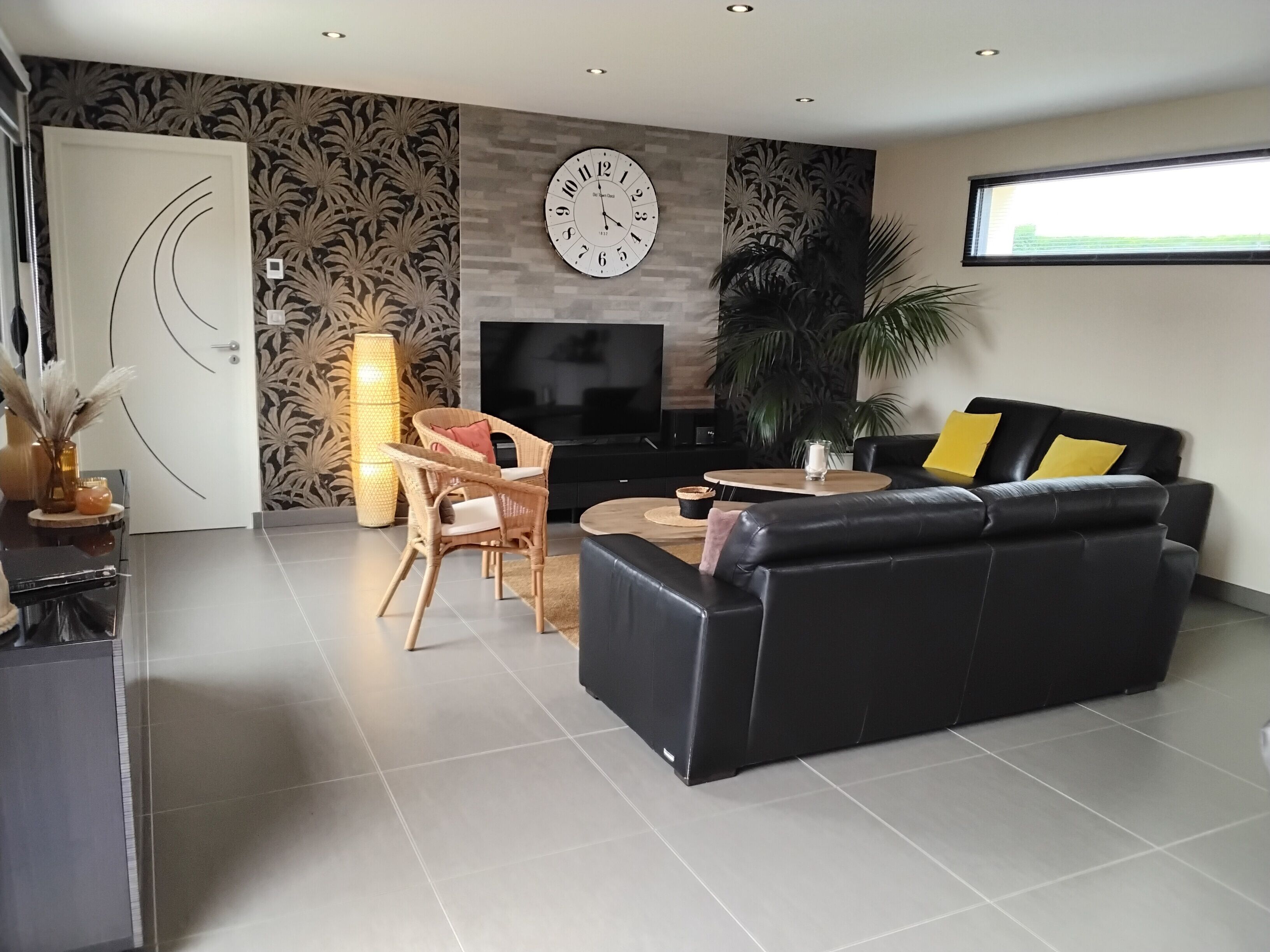 Un salon moderne avec un canapé en cuir noir, une table basse ronde, un téléviseur et une grande horloge murale.