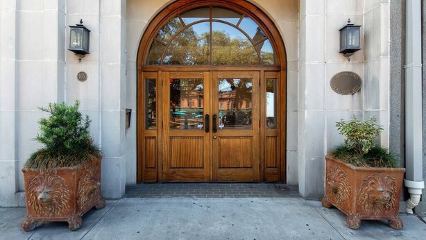 A double wooden door with glass panels, flanked by two lion-shaped planters, and a stone plaque above the door. - Step into a spacious, luxury condo that has it all – a premiere location in the heart of the Historic District and floor-to-ceiling window views of the Savannah River, Talmadge Bridge and City Hall. 5th floor.Best river views in the building. (Savannah)