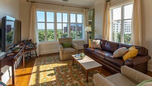 A living room with a brown leather sofa, a beige armchair, a wooden coffee table, and a patterned rug. - Step into a spacious, luxury condo that has it all – a premiere location in the heart of the Historic District and floor-to-ceiling window views of the Savannah River, Talmadge Bridge and City Hall. 5th floor.Best river views in the building. (Savannah)