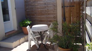 A patio area with a round table and two chairs, surrounded by wooden fences and potted plants. - Charming studio, quiet, patio, 2-4p (Fontvieille)