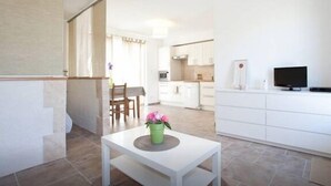 A modern kitchen with white cabinets, a dining area with a table and chairs, and a TV on a stand. - Charming studio, quiet, patio, 2-4p (Fontvieille)