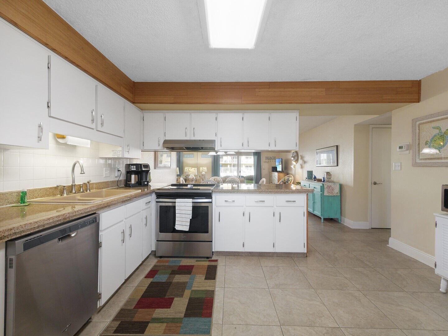 A modern kitchen with white cabinets, stainless steel appliances, and a colorful rug.
