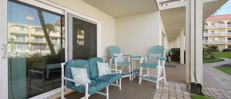 A balcony with a sofa and chairs, a sliding glass door, and a view of a building with balconies.