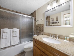 Une salle de bain dotée d’une douche à parois de verre, de toilettes blanches, d’un lavabo avec un meuble-vasque et d’un miroir au-dessus du lavabo.