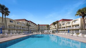 A swimming pool surrounded by a multi-story hotel with balconies and palm trees.