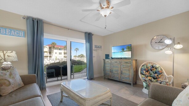 A living room with a glass-top table, two sofas, a television, a clock, and a ceiling fan.