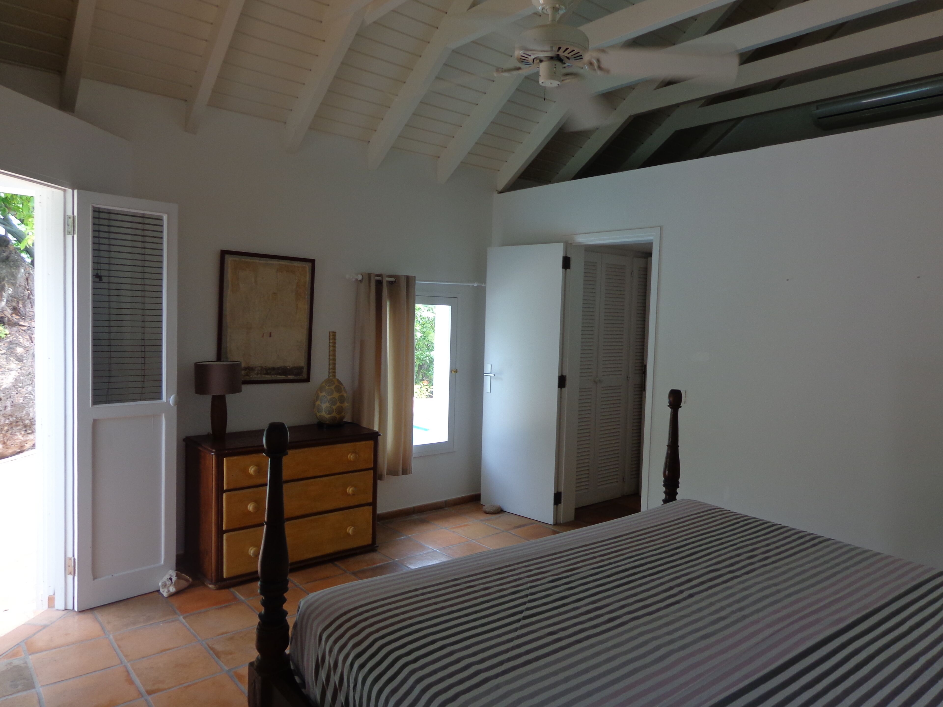 Quarto com cama, cômoda e porta que dá para outro espaço.