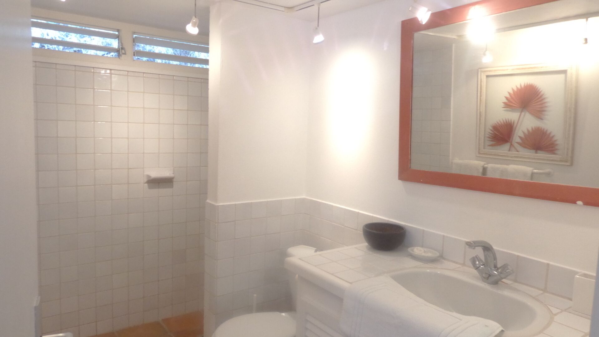 A bathroom with a shower, toilet, sink, and a mirror with a decorative frame.