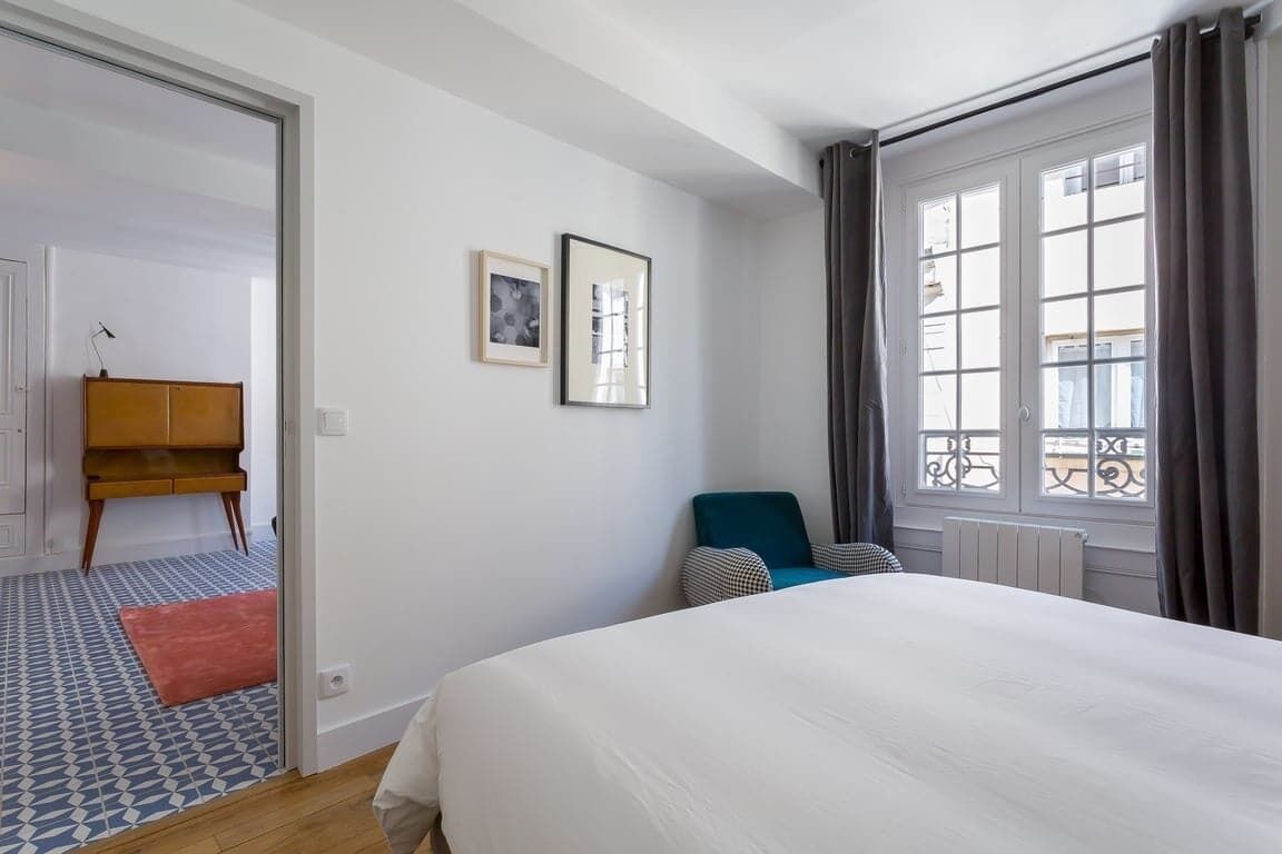Une chambre d’hôtel avec un lit, une chaise, un bureau et une fenêtre avec des rideaux.
