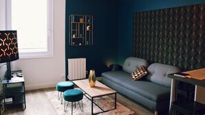Ein modernes Wohnzimmer mit grauem Sofa, Türkis-farbenen Hocker, einem Holztisch und strukturierter Wandgestaltung.