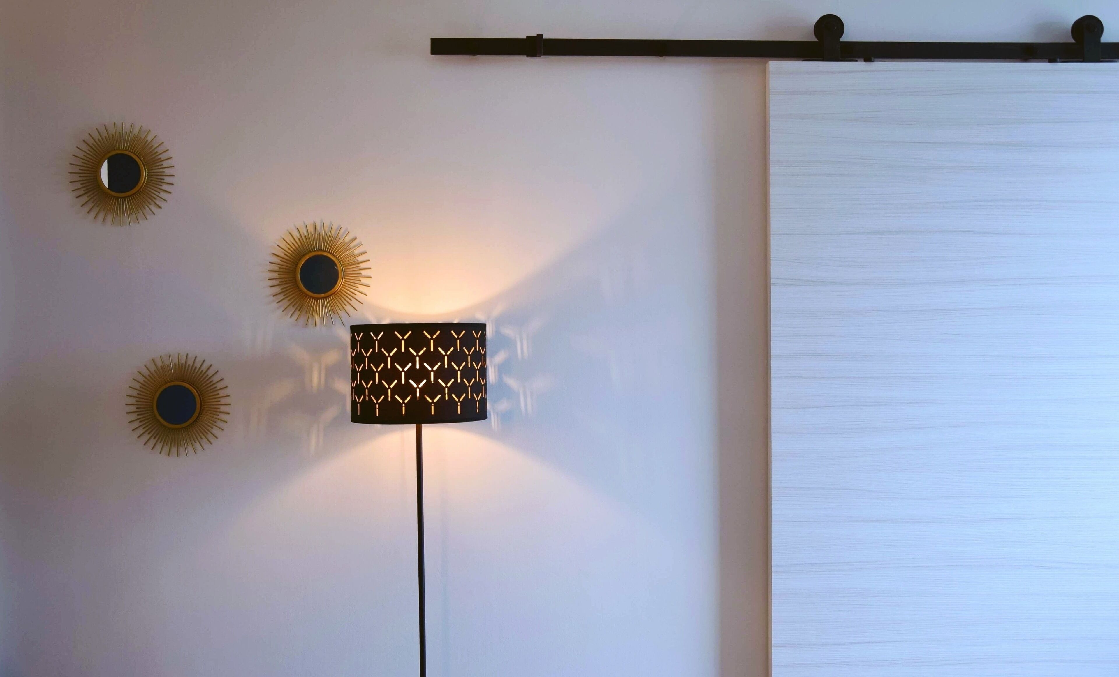 Un mur orné de trois appliques murales en forme de soleil et d’un luminaire moderne aux motifs géométriques.