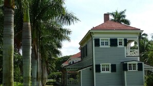 A two-story house with a balcony, surrounded by a well-maintained lawn and palm trees. - Book now and save: great deals for your next getaway! (Cape Coral)