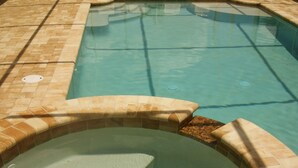 A hot tub with a tiled edge, a drain, and a pool in the background. - Book now and save: great deals for your next getaway! (Cape Coral)
