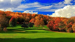 Un campo de golf con un club de campo, rodeado de árboles de colores otoñales y un cielo azul despejado.