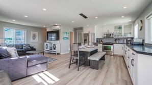 Eine moderne Küche mit weißen Schränken, ein Essbereich mit einer Bank und ein Wohnzimmer mit Sofa und Fernseher.