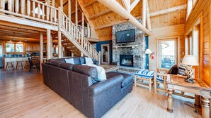 Amplia sala de estar con chimenea de piedra, un sofá marrón grande y una escalera de madera.