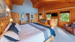 Un dormitorio de cabaña de madera con una cama grande, un aparador, una silla y un televisor.