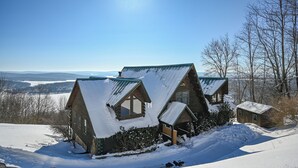 Una cabaña con techo inclinado, rodeada de suelo y árboles cubiertos de nieve, con una vista despejada del paisaje al fondo.