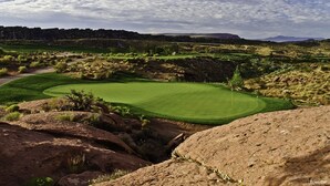 Een golfbaan met een helder zicht op de green, de fairways en het omliggende rotsachtige landschap.