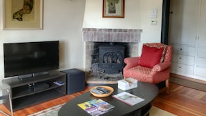 A living room with a fireplace, a television, a red armchair, and framed artwork on the wall. - Just blocks from UC, Simons, MSRI, Haas and Goldman Schools with great Bay views (Berkeley)
