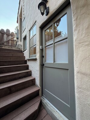 A building with a grey door, a window with blinds, and a wooden staircase leading to the entrance. - Just blocks from UC, Simons, MSRI, Haas and Goldman Schools with great Bay views (Berkeley)