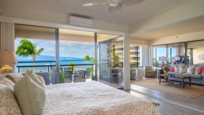 Camera d'albergo con un letto grande, un balcone vista oceano e una zona soggiorno con divano e tavolino.