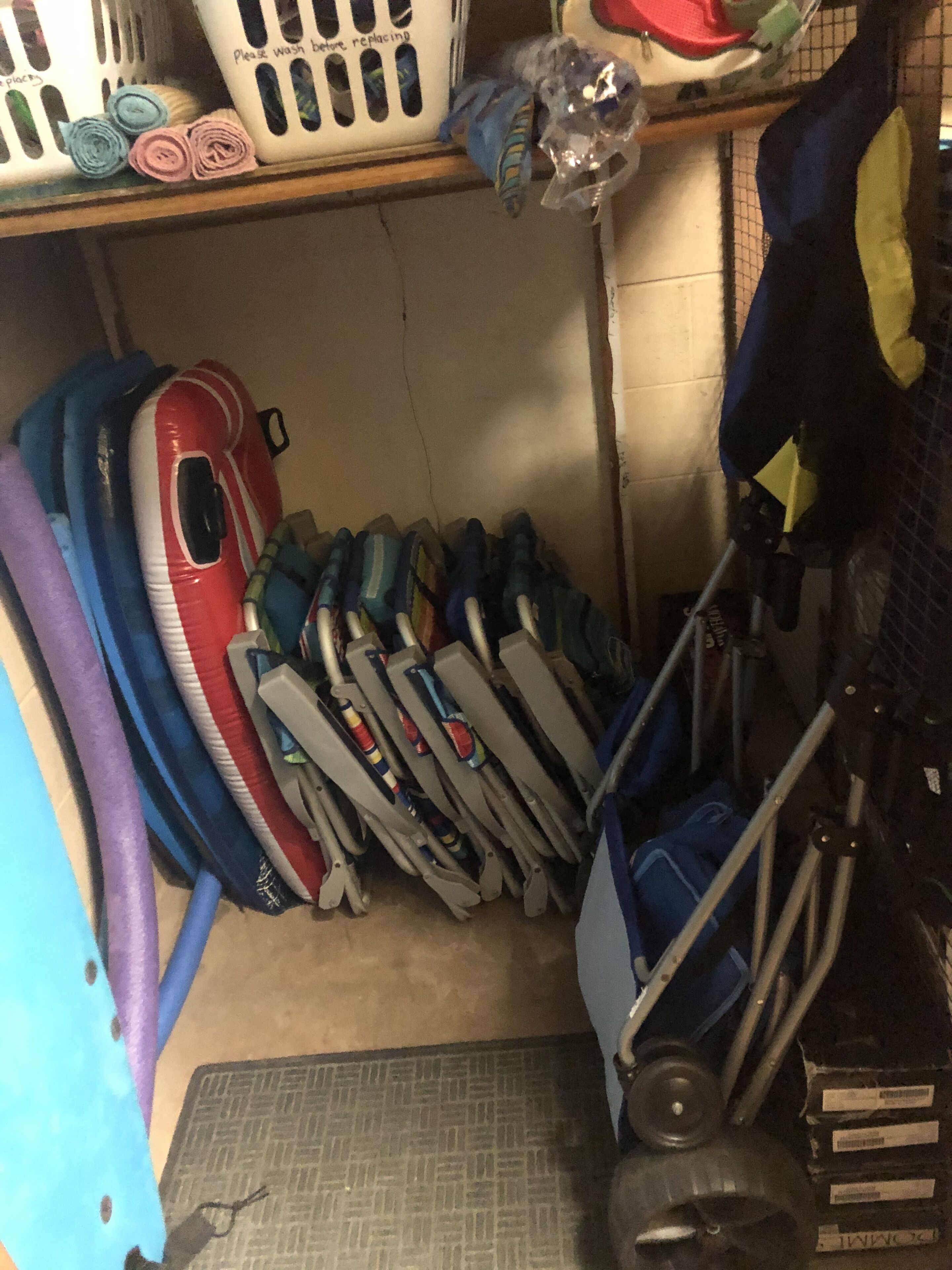 A storage area with various items including rolled-up mats, a red and white inflatable, and a blue and yellow kayak.