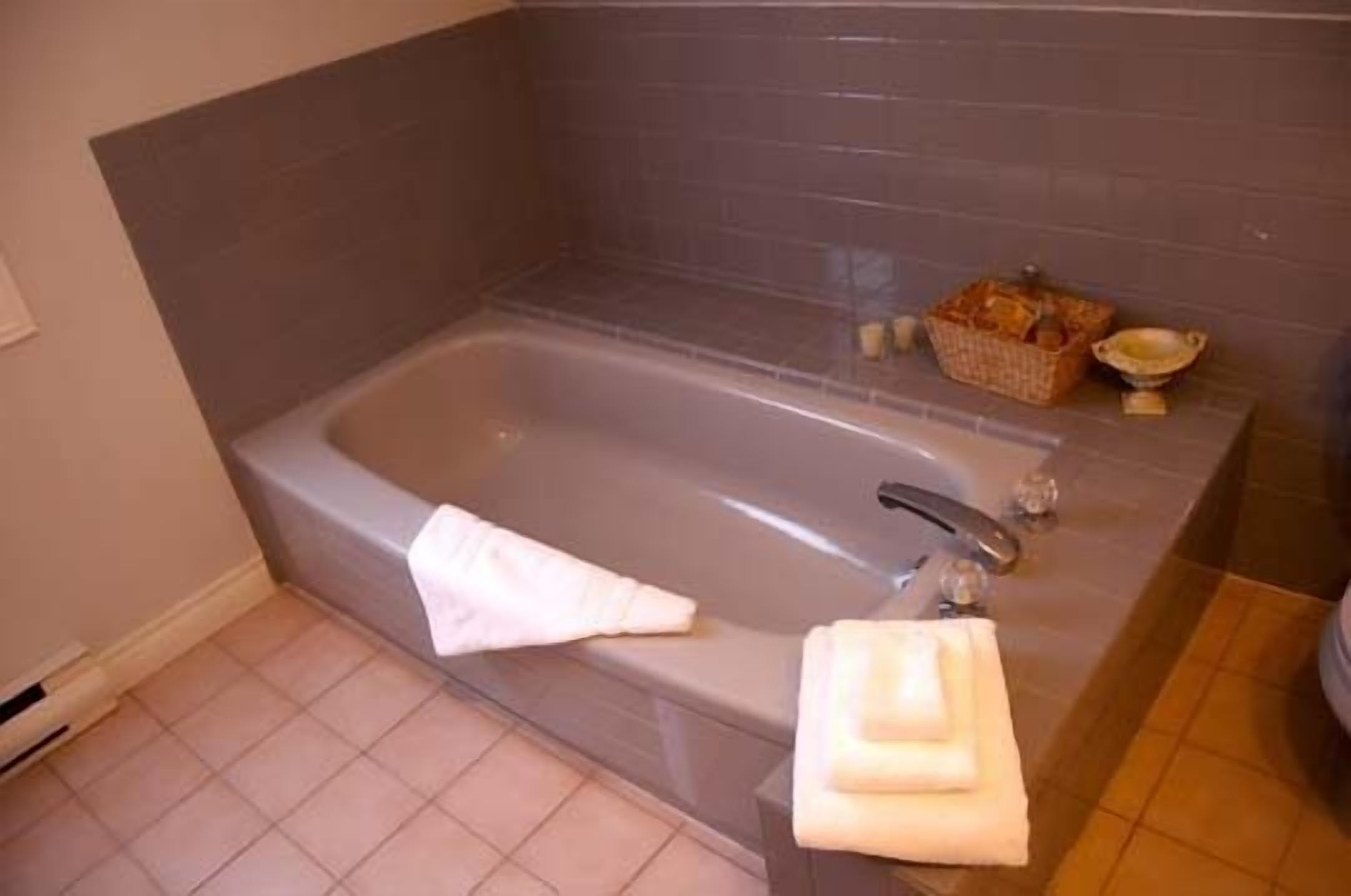 A bathroom with a bathtub, a towel rack, and a basket of toiletries.