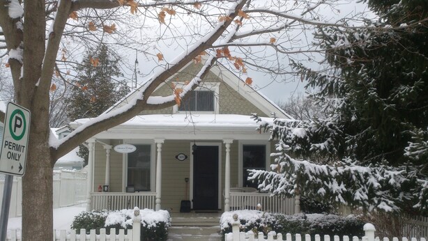 Une maison recouverte de neige, avec une clôture blanche en bois, un porche et un panneau indiquant qu’il s’agit d’une zone de stationnement réservée aux personnes autorisées.