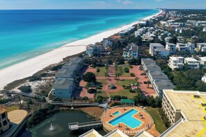 An aerial view of a coastal resort with a swimming pool, beachfront, and multiple buildings.
