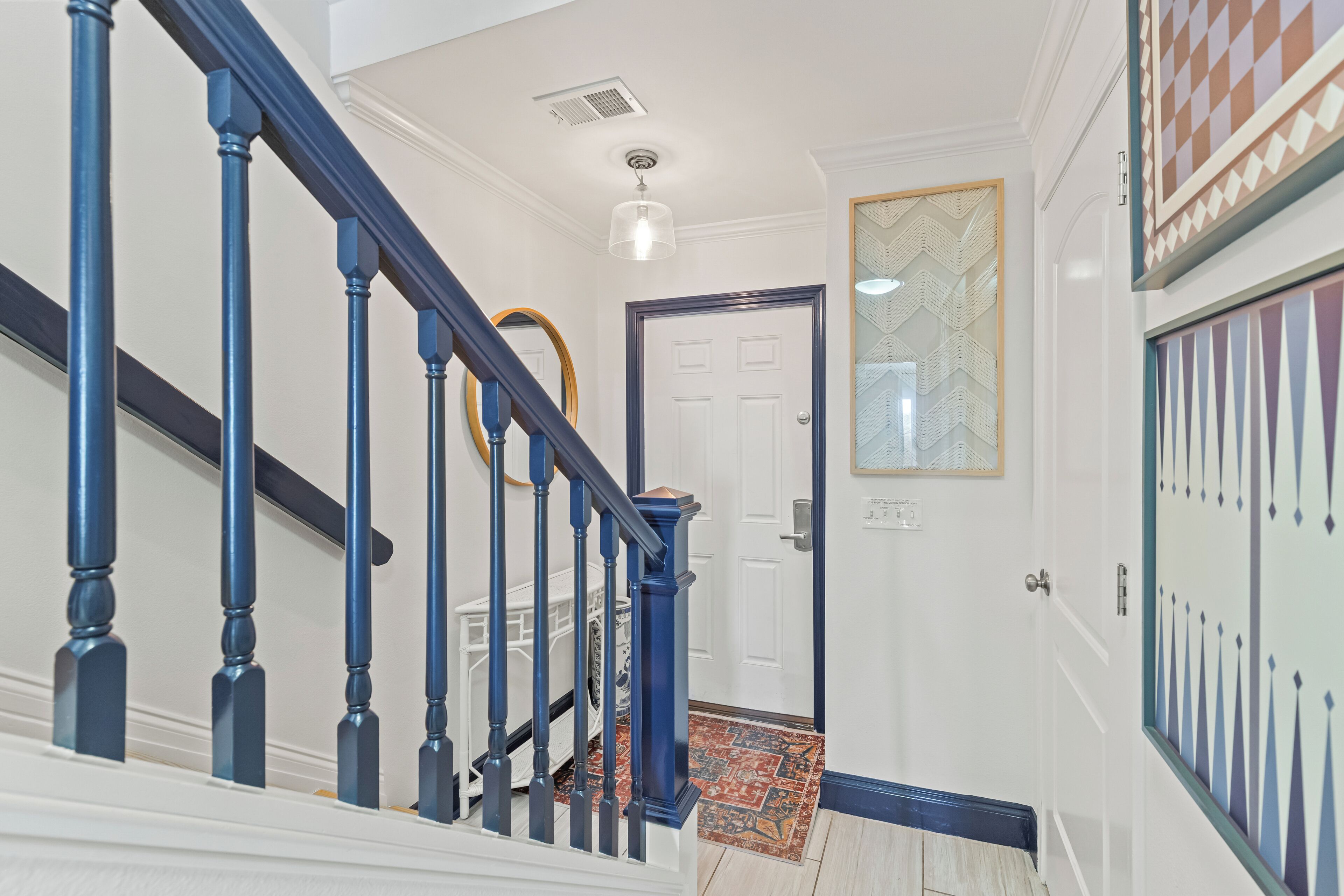 Un escalier avec des balustrades bleues et des murs blancs, menant à une porte ornée d’un panneau de verre à motifs.