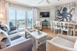 Relax in a comfortable living space with a sofa, armchair, and TV, opening up to a serene ocean-view balcony.