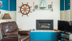 Un salon avec une cheminée, un téléviseur, un fauteuil en cuir et des éléments de décoration sur le thème de la marine.