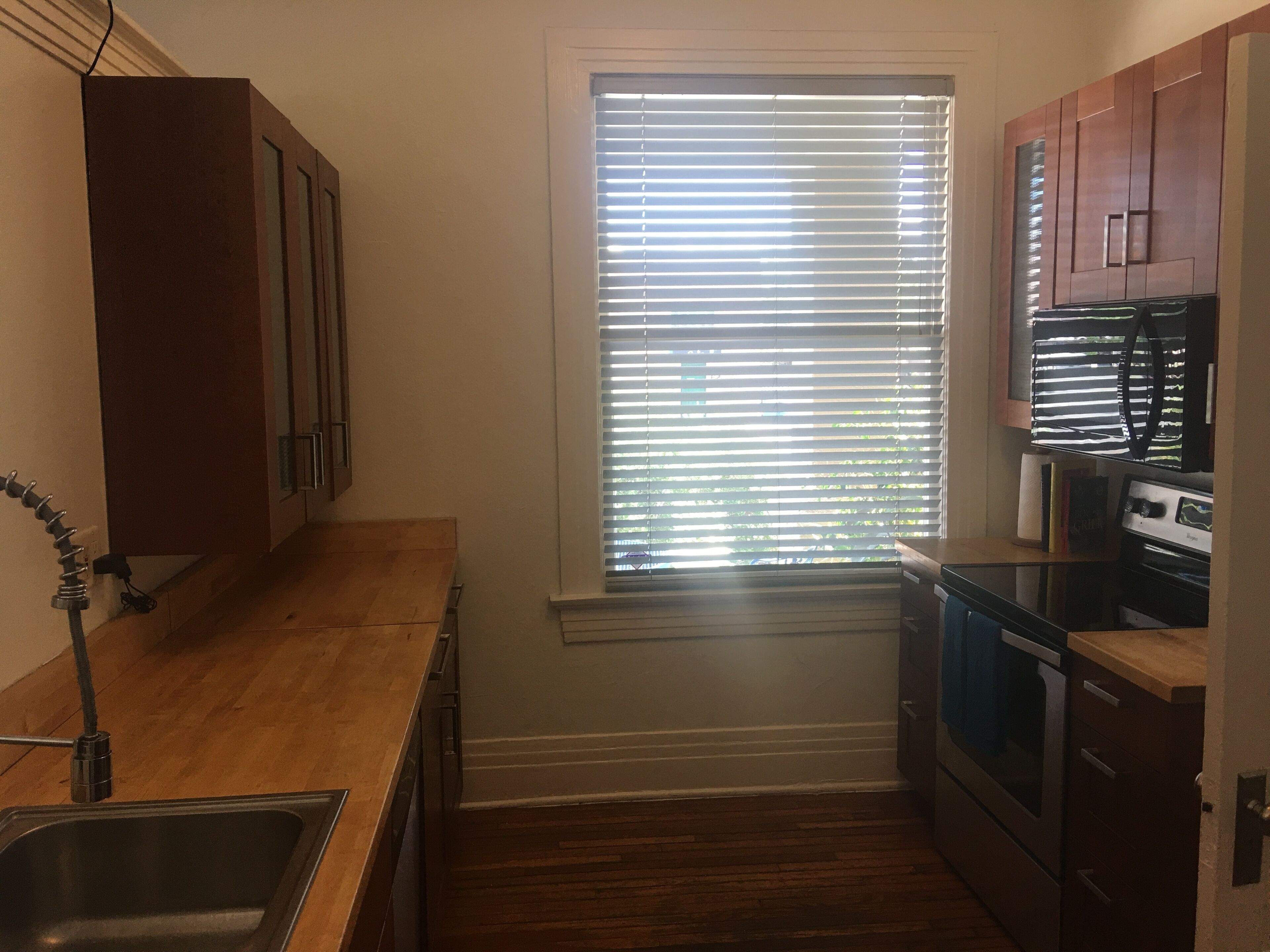 A small kitchen with wooden cabinets, a window with blinds, a sink, and a stove.
