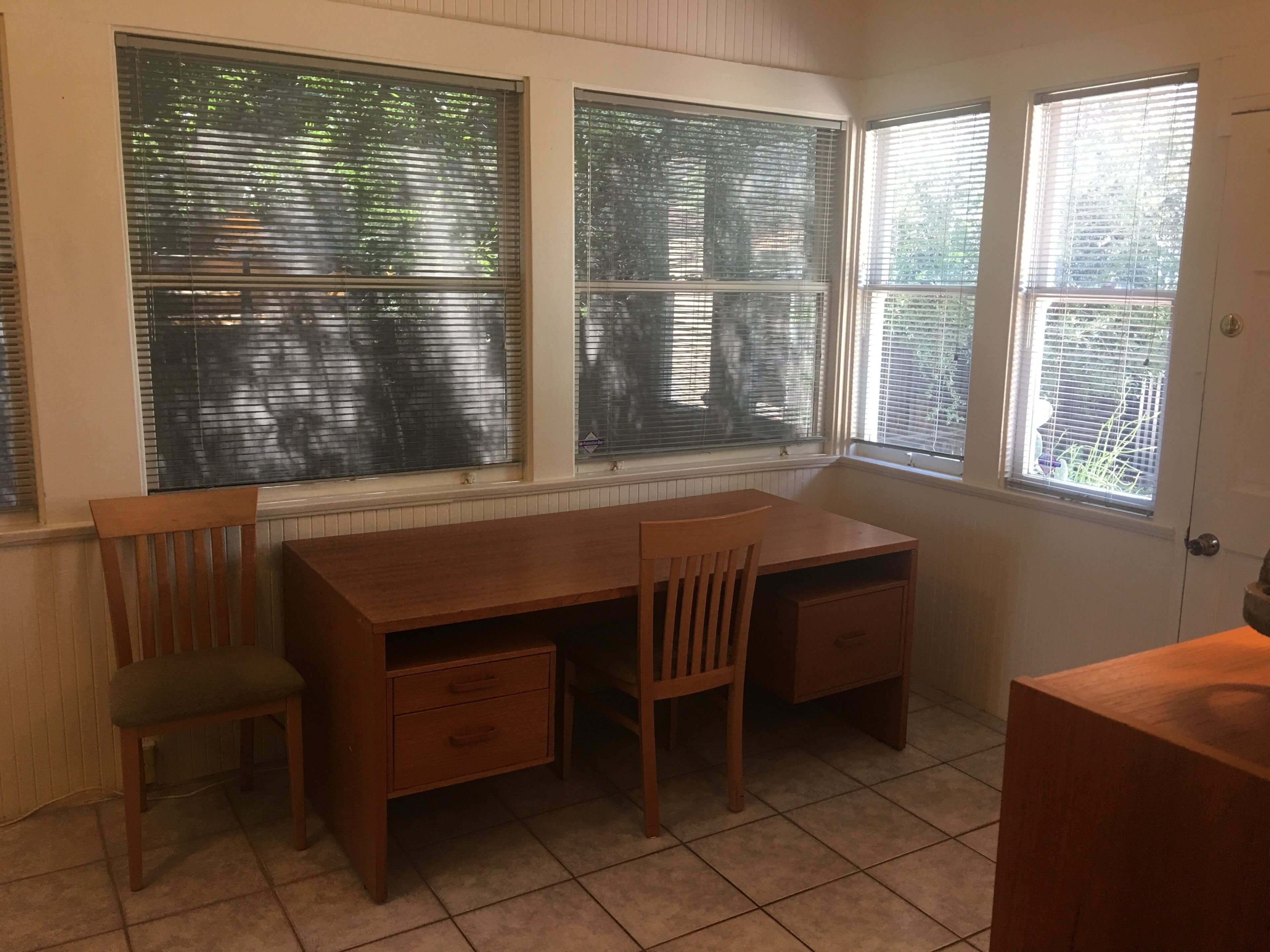 Una habitación con escritorio de madera, dos sillas y una ventana con persianas.