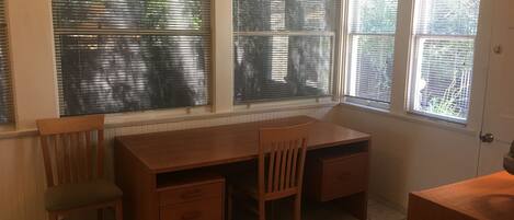 Una habitación con escritorio de madera, dos sillas y una ventana con persianas.