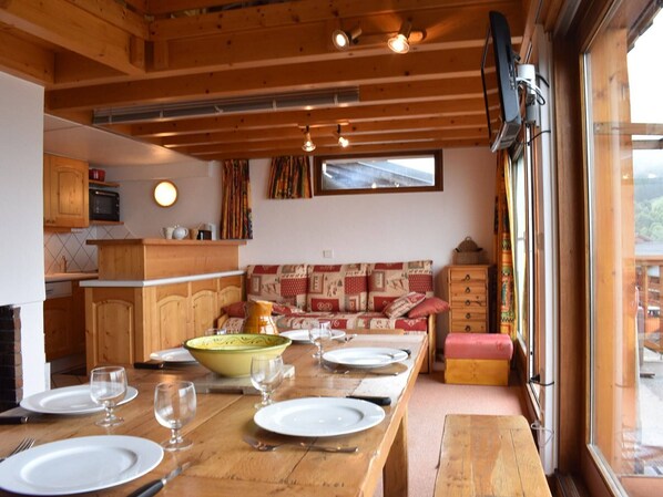 L’intérieur chaleureux d’un chalet comprend une table à manger en bois, préparée pour quatre personnes, un canapé et un coin cuisine équipé d’un four à micro-ondes et de placards.
