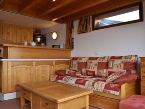 L’intérieur chaleureux d’un chalet avec un banc en bois, un canapé matelassé et un coin cuisine doté de meubles en bois et d’un four à micro-ondes.