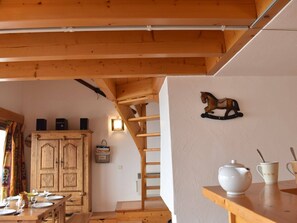 Interior de madeira com uma mesa de jantar posta para quatro pessoas, um armário de madeira e uma decoração de cavalo na parede.