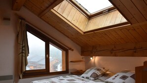 A bedroom with a skylight, a large window, a bed with a quilt, and a nightstand. - Cozy 2-Room Mezzanine Apartment for 6 in Méribel Center, 200m from Slopes (Méribel)