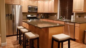 Eine moderne Küche mit Holzausstattung, Edelstahlgeräten, einer Granitarbeitsplatte und Barhocker.
