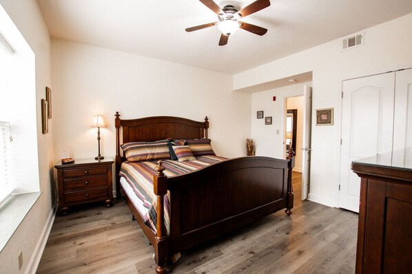 A bedroom with a wooden bed, a nightstand with a lamp, a ceiling fan, and a door leading to another room. - Making Memories - Unit 3301 - FREE Attraction Ticket with EACH night Stay Including Dollywood (Pigeon Forge)
