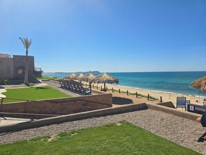A beachside view with a clear sky, a palm tree, and a building with a stone facade.