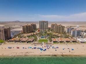 A resort with multiple high-rise buildings, a central pool, and a beach area with umbrellas. - 3BR Villa w/ Rooftop Sea Views Steps to Beach (Puerto Peñasco)