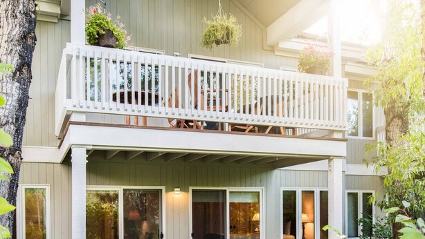 Une maison à deux étages avec un balcon, une véranda avec des chaises et un petit jardin.