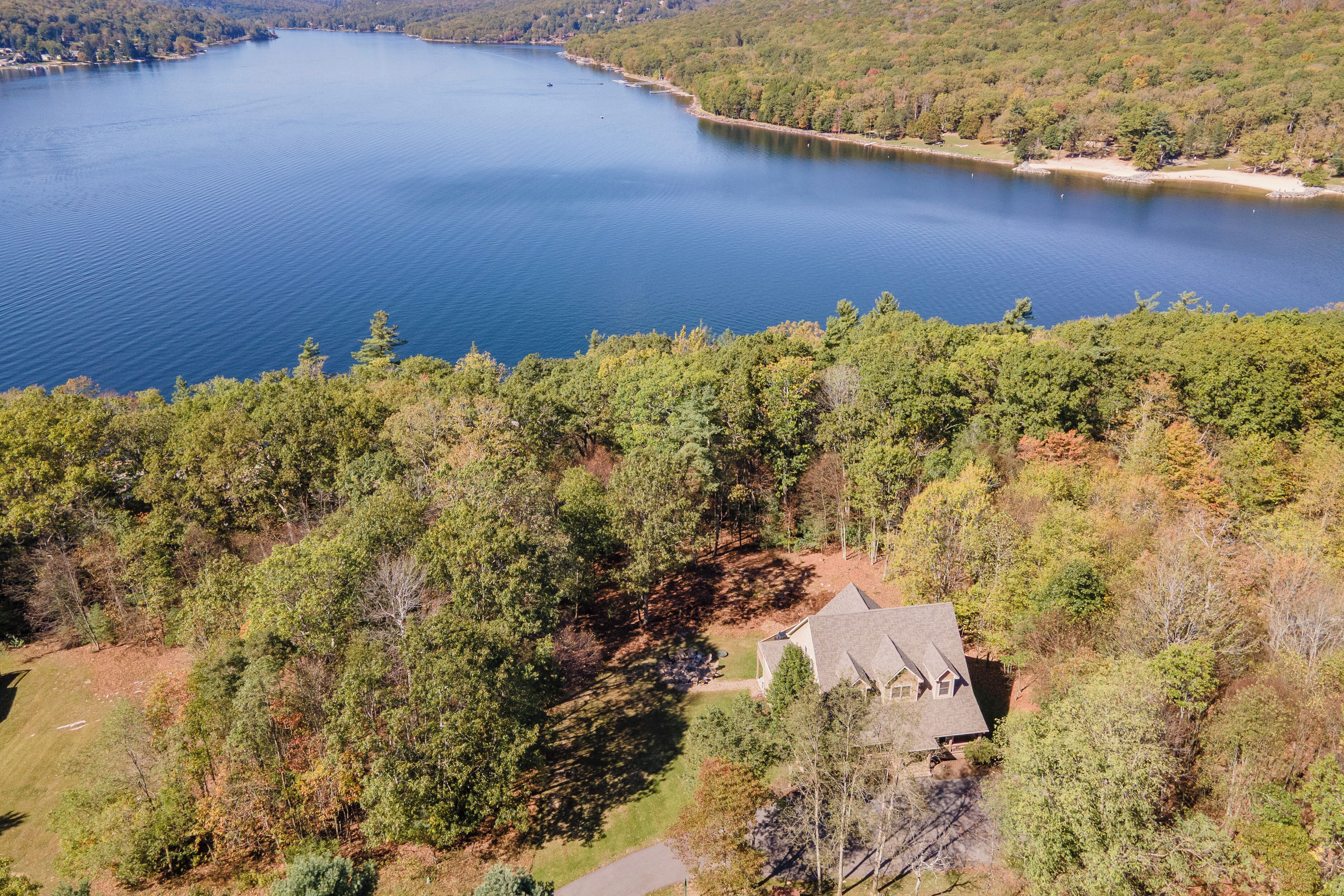 A lake surrounded by dense forest, a house with a sloped roof, and a clear sky.