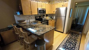 A kitchen with wooden cabinets, stainless steel appliances, a granite countertop, and a patterned rug. - Private deck, BBQ Grill, view of golf course (Eden)