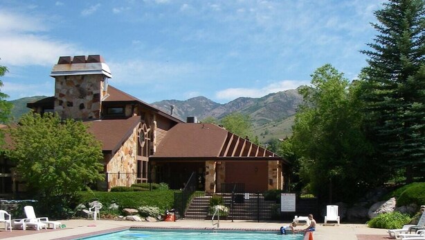A pool area with a stone building, lounge chairs, and mountains in the background. - Private deck, BBQ Grill, view of golf course (Eden)
