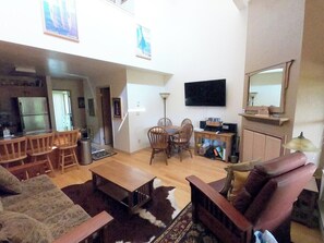 A spacious living room with a dining area, a kitchen, and a TV mounted on the wall.