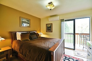 A bedroom with a bed, bedside lamps, a window, and a balcony with chairs.